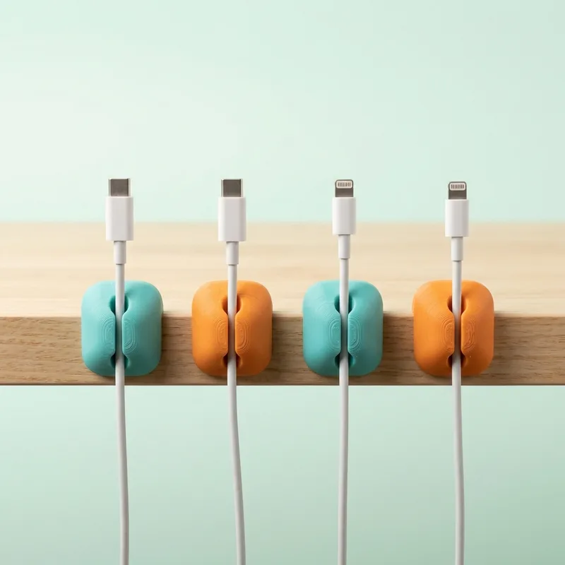 Cuatro clips para cables en colores turquesa y naranja pegados al borde de un escritorio